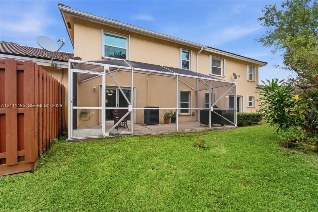 Rear exterior featuring a screened-in lanai, concrete patio, stucco siding, and wood-panel fencing