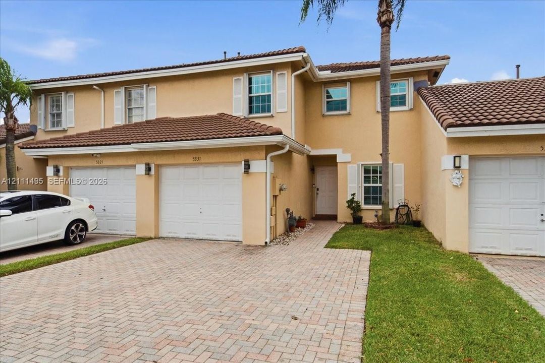 Two-story exterior featuring a stucco facade, tile roof, three-car garage, and paver driveway