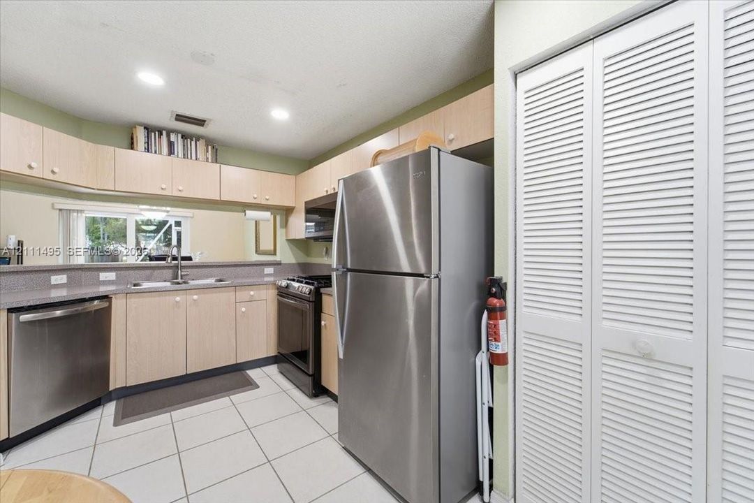 Kitchen featuring stainless steel appliances, light wood-finish cabinetry, tile flooring, and white louvered closet doors