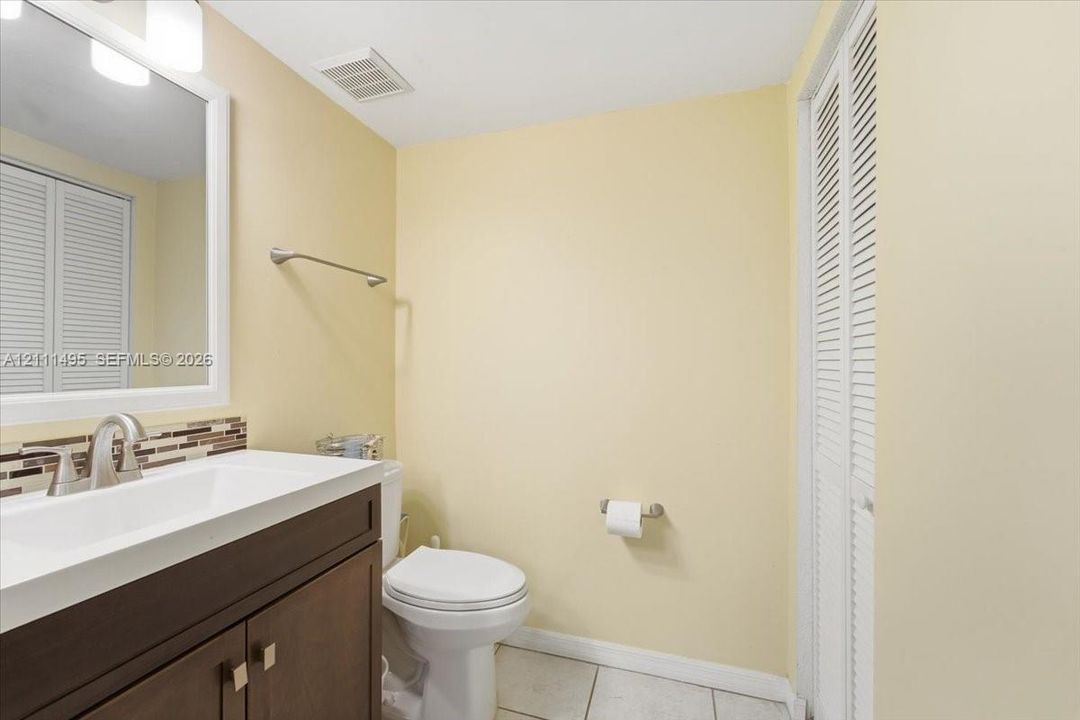 Bathroom featuring a vanity with a white rectangular sink, stone-finish countertop, dark wood-finish cabinetry, a white-framed mirror, and bi-fold louvered closet doors
