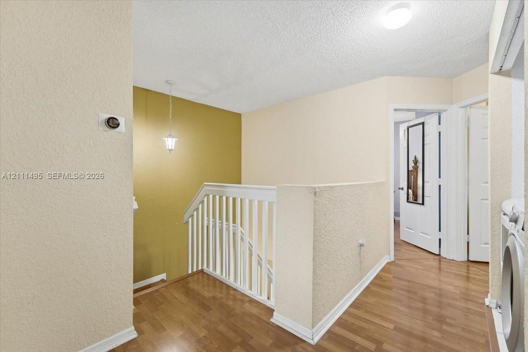 Staircase featuring wood-finish flooring, white spindle railing, flush-mount ceiling lighting, and pendant light fixture