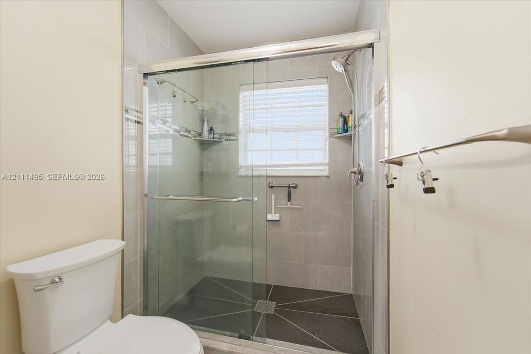 Walk-in shower featuring a sliding glass enclosure, neutral wall tile, dark floor tile, and polished chrome shower hardware
