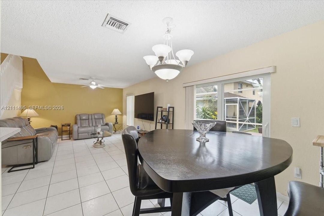 Open interior space featuring light-colored tile flooring, a multi-arm overhead chandelier, a ceiling fan with integrated lighting, and sliding glass doors