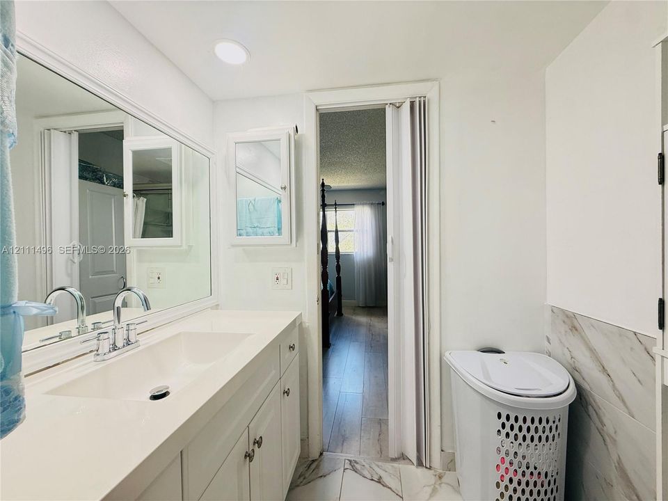 Bathroom featuring a white vanity cabinet with an integrated sink, a large wall-mounted mirror, recessed lighting, and stone-finish floor tiling