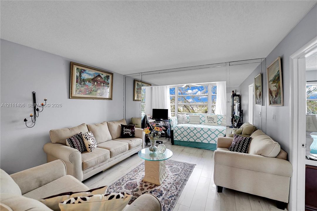 Living area featuring light-toned wood-finish flooring, floor-to-ceiling wall mirrors, and large windows