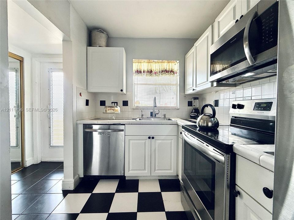 Kitchen featuring white cabinetry, stainless steel appliances, tile backsplash, and checkerboard flooring