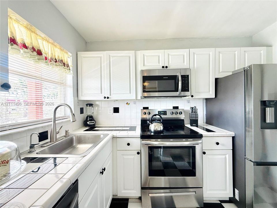 Kitchen featuring white shaker-style cabinetry, stainless steel appliances, tile countertops, and a stainless steel undermount sink with a gooseneck faucet