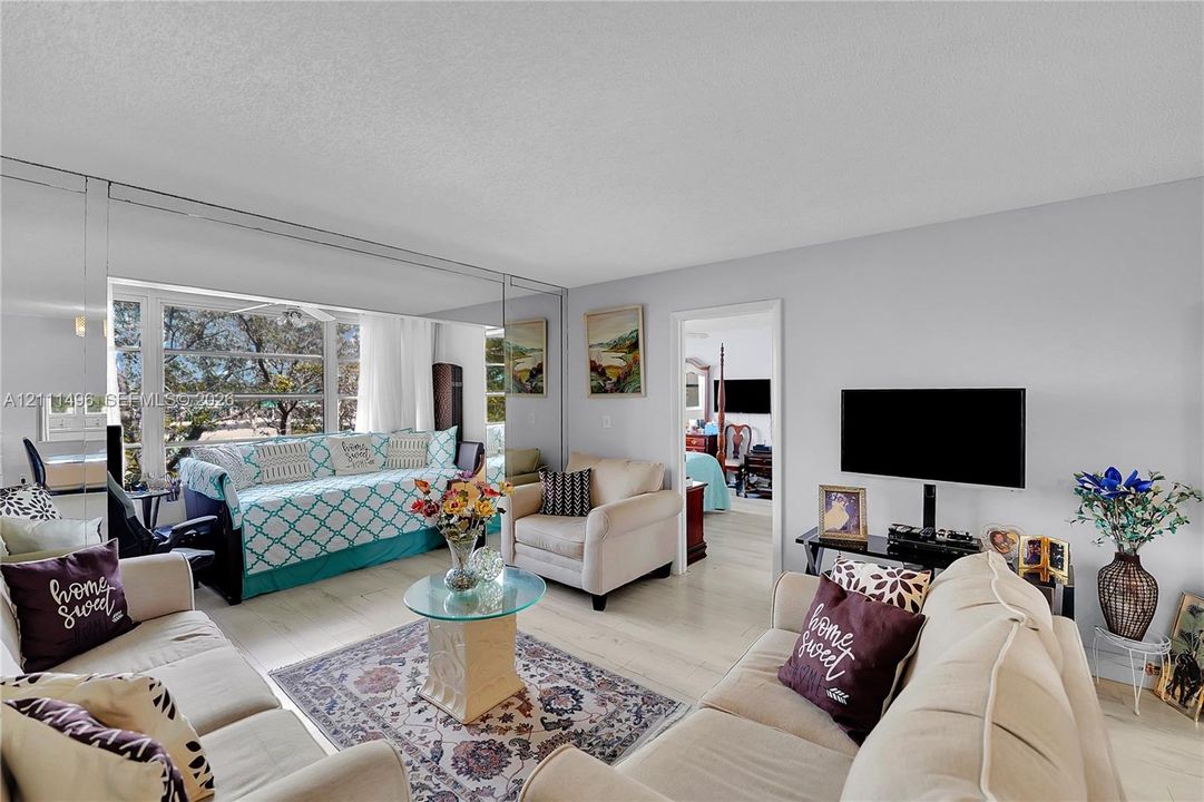Living area featuring light-toned wood-finish flooring, floor-to-ceiling mirrored wall panels, and expansive windows