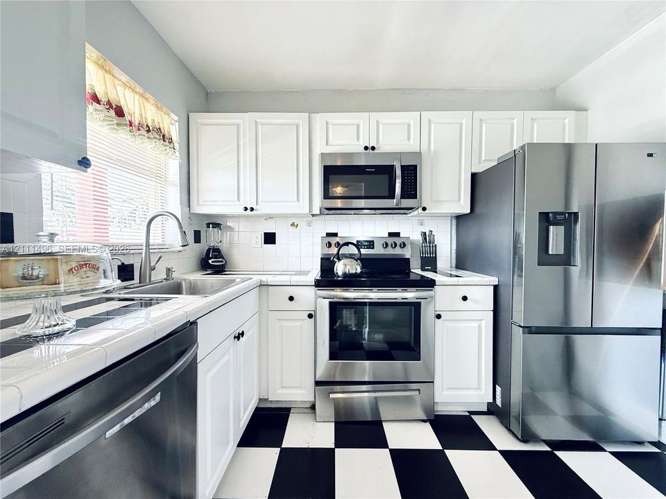 Kitchen featuring white cabinetry, stainless steel appliances, tiled countertops, and black-and-white checkered flooring