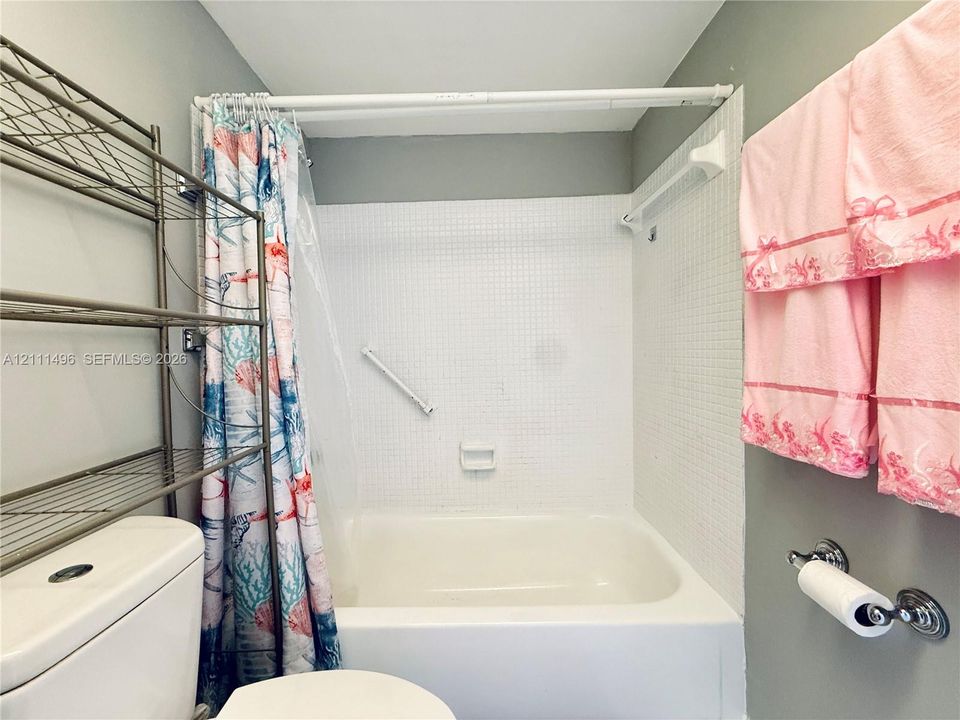 Bathtub with white mosaic wall tile surround, integrated soap dish, and wall-mounted grab bar, complemented by a metal toilet paper holder
