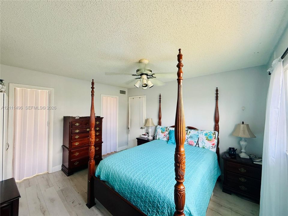 Room featuring wood-finish flooring, textured ceiling, central ceiling fan with multi-light fixture, and dual folding closet doors