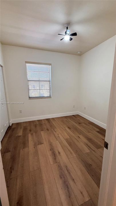 Interior space featuring wood-finish flooring, a neutral wall palette, a single window with horizontal blinds, and a central ceiling fan with an integrated light fixture
