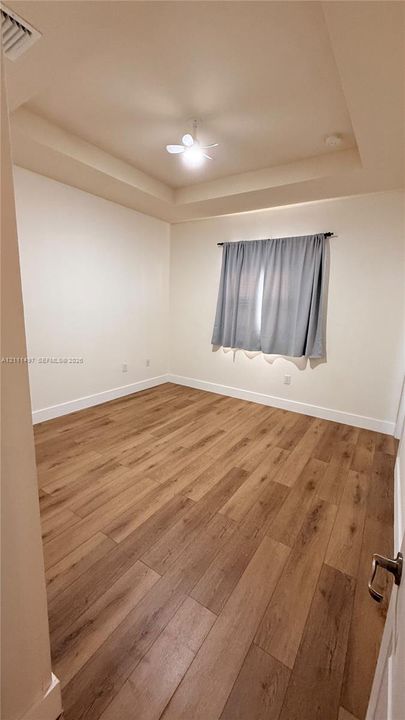 Tray ceiling featuring a recessed center, wood-finish flooring, and a central ceiling fan with an integrated light fixture