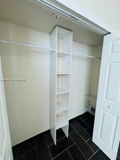 Closet featuring built-in vertical shelving, dual hanging rods, wire storage rack, and dark tile flooring