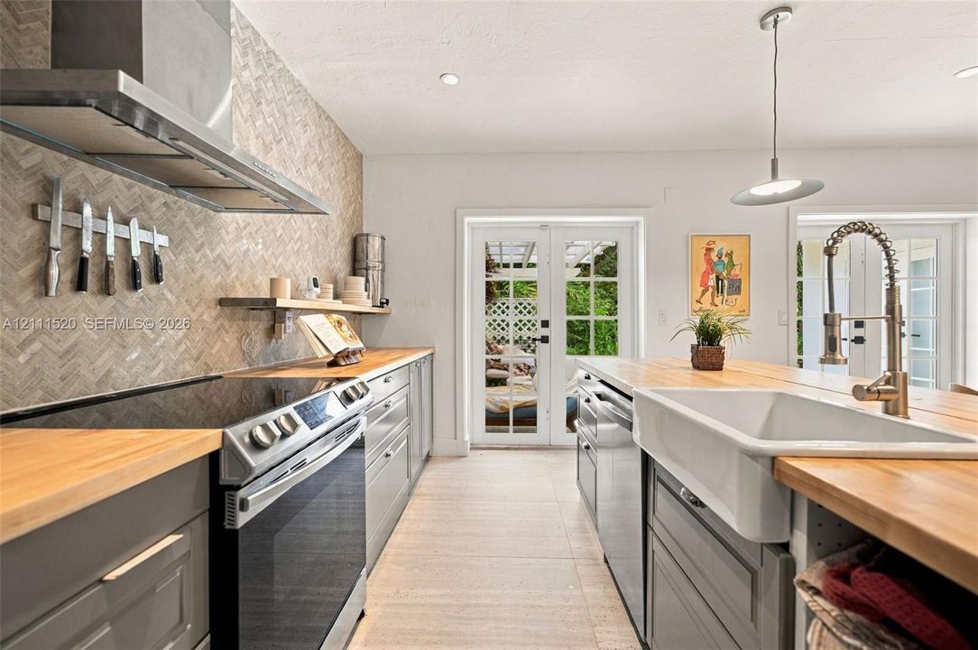 Kitchen featuring butcher block countertops, a farmhouse-style apron sink, a herringbone-patterned tile backsplash, stainless steel appliances, and French doors