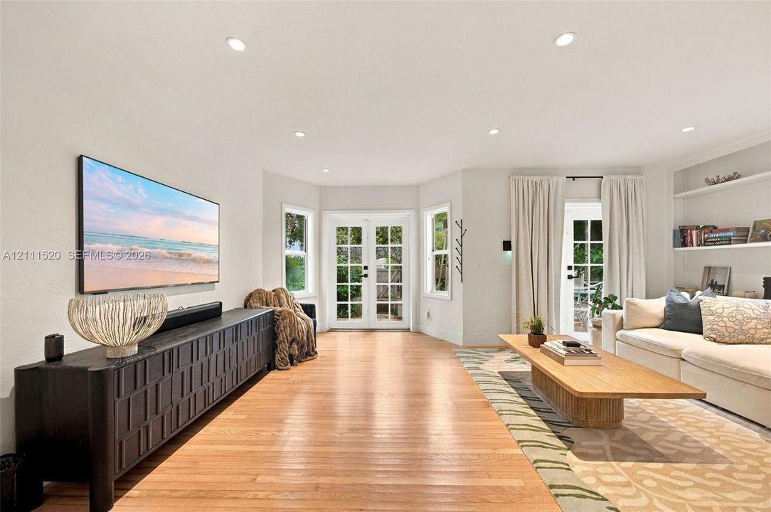 Living area featuring wood-finish flooring, recessed lighting, double French doors, and built-in shelving