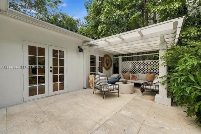 Patio featuring large-format light-toned stone paving, white wood pergola, lattice privacy screening, and white-framed multi-lite glass panel doors