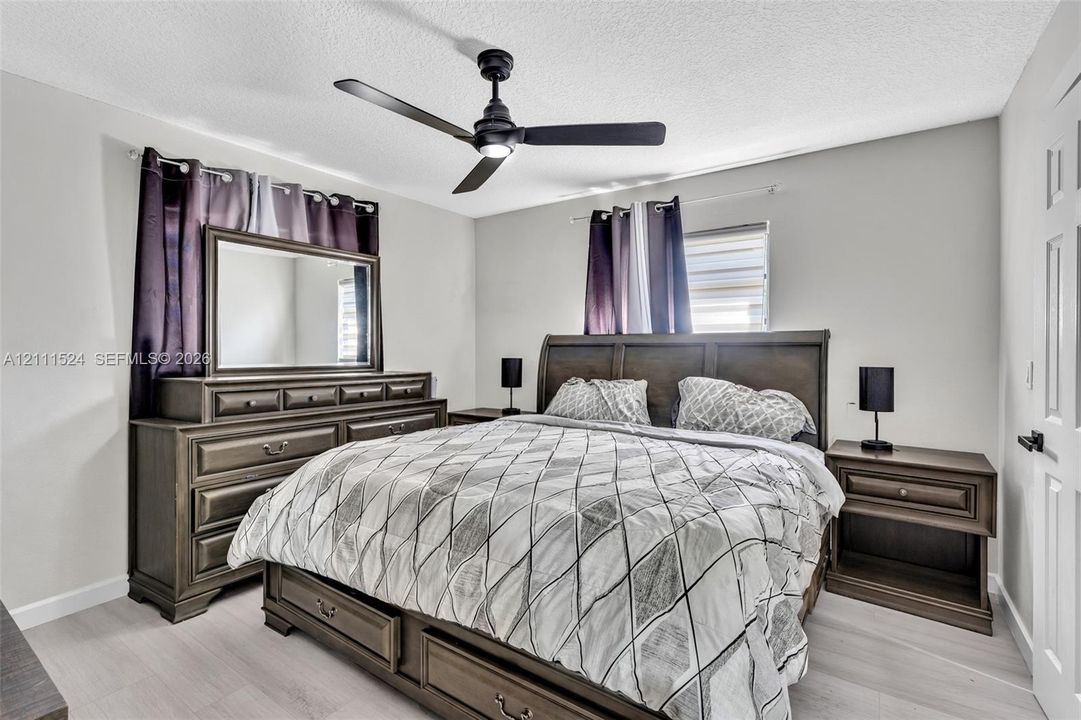 Light-toned wood-finish flooring, ceiling-mounted matte black fan, and multi-panel interior door with matte black hardware