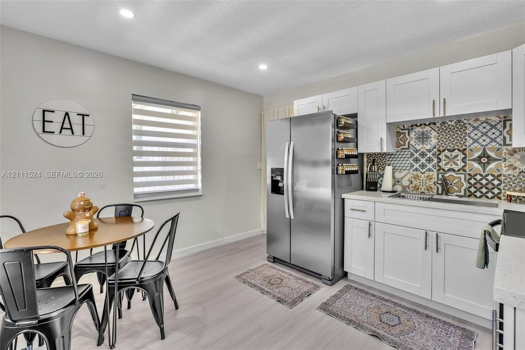 Kitchen featuring white shaker-style cabinetry, patterned tile backsplash, stainless steel refrigerator, light-toned wood-finish flooring, and recessed lighting