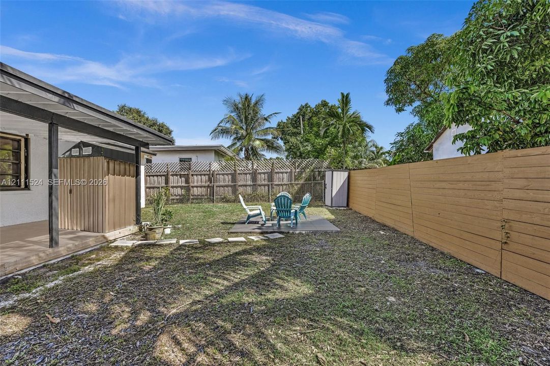Fenced backyard featuring a covered patio, paved seating area, metal storage shed, and mature perimeter trees