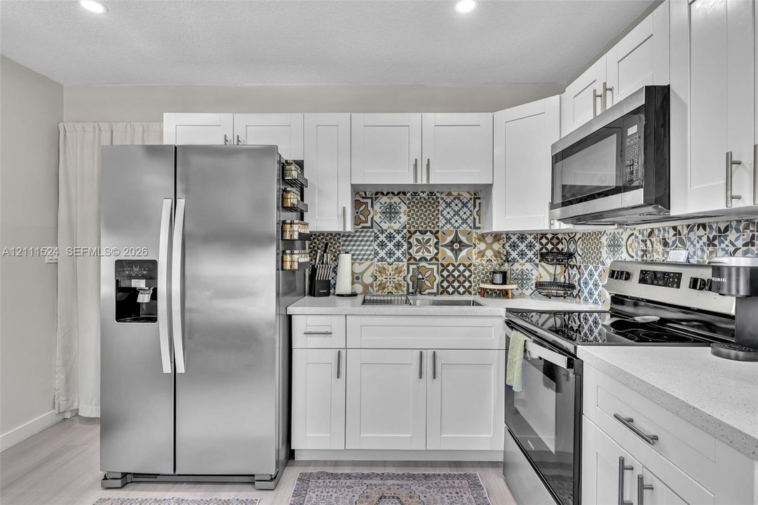 Kitchen featuring white shaker-style cabinetry, stainless steel appliances, patterned tile backsplash, solid-surface countertops, and recessed lighting