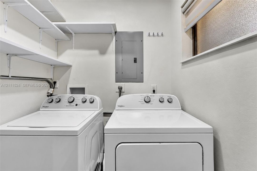 Laundry area featuring white tiered wall shelving, a wall-mounted hook rack, and a frosted window
