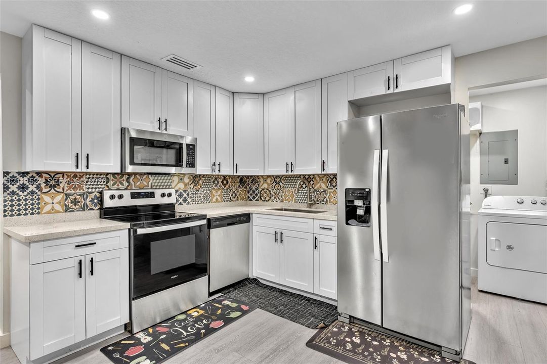 Kitchen featuring white shaker-style cabinetry, patterned tile backsplash, stainless steel appliances, and solid surface countertops