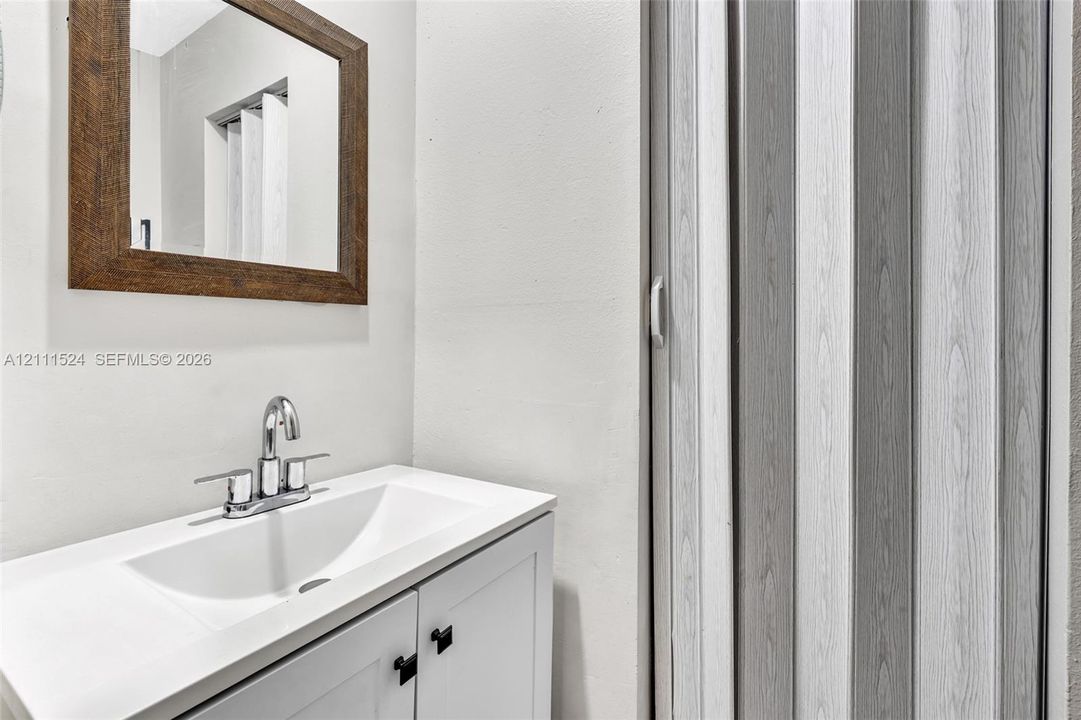 White vanity cabinet with integrated basin and polished chrome dual-handle faucet, complemented by a wood-frame wall mirror and vertical-panel sliding door