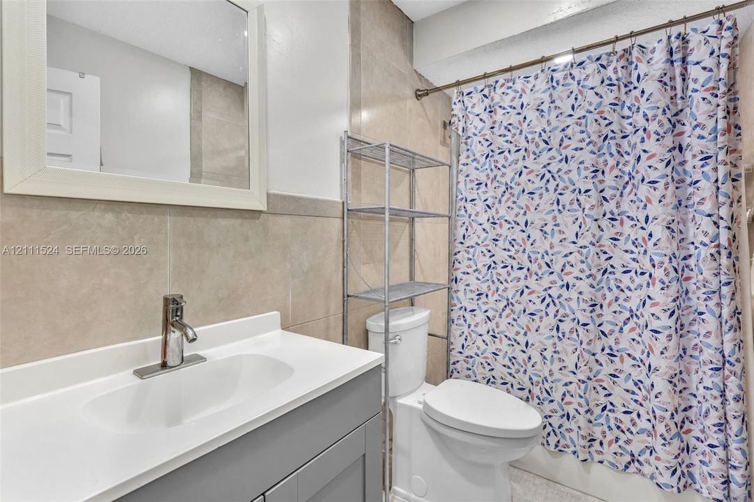 Bathroom featuring a vanity with a white countertop and integrated sink, chrome faucet, framed mirror, and tile wall surround