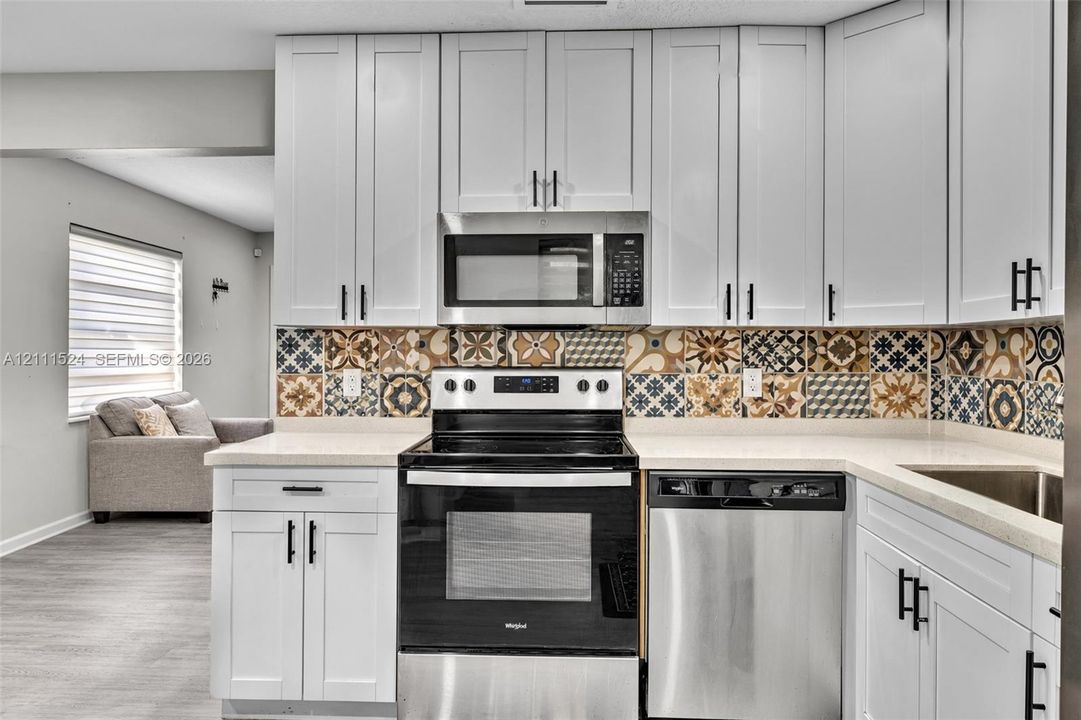 Kitchen featuring white Shaker-style cabinetry, patterned tile backsplash, neutral countertops, and stainless steel appliances