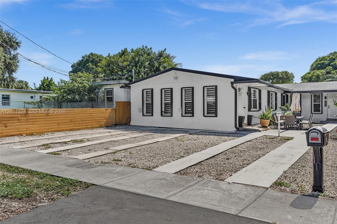 Single-story residence featuring a painted exterior, horizontal wood-slat fencing, multiple windows with dark trim, and a gravel driveway with concrete parking strips