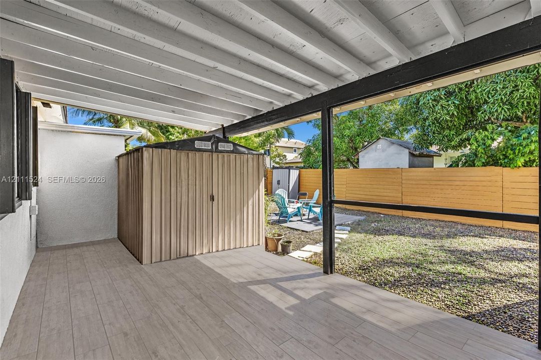Covered patio featuring wood-finish tile flooring and an exposed beam ceiling, overlooking a fenced backyard with gravel and grass ground cover