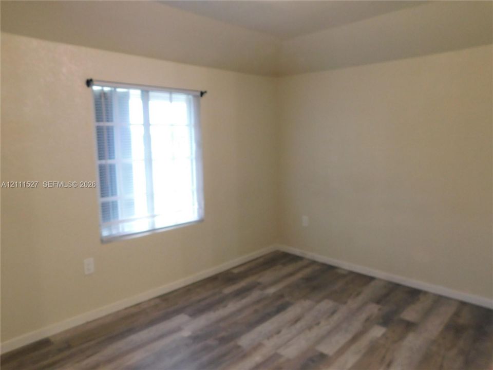 Room featuring wood-finish flooring, neutral-toned walls, and a multi-pane window with a frame-mounted blind. Master bedroom