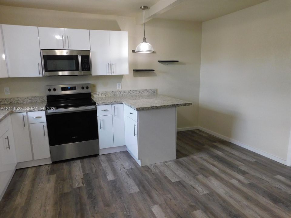 Kitchen featuring white flat-panel cabinetry, stone-finish countertops, stainless steel appliances, wood-finish flooring, and wall-mounted shelving