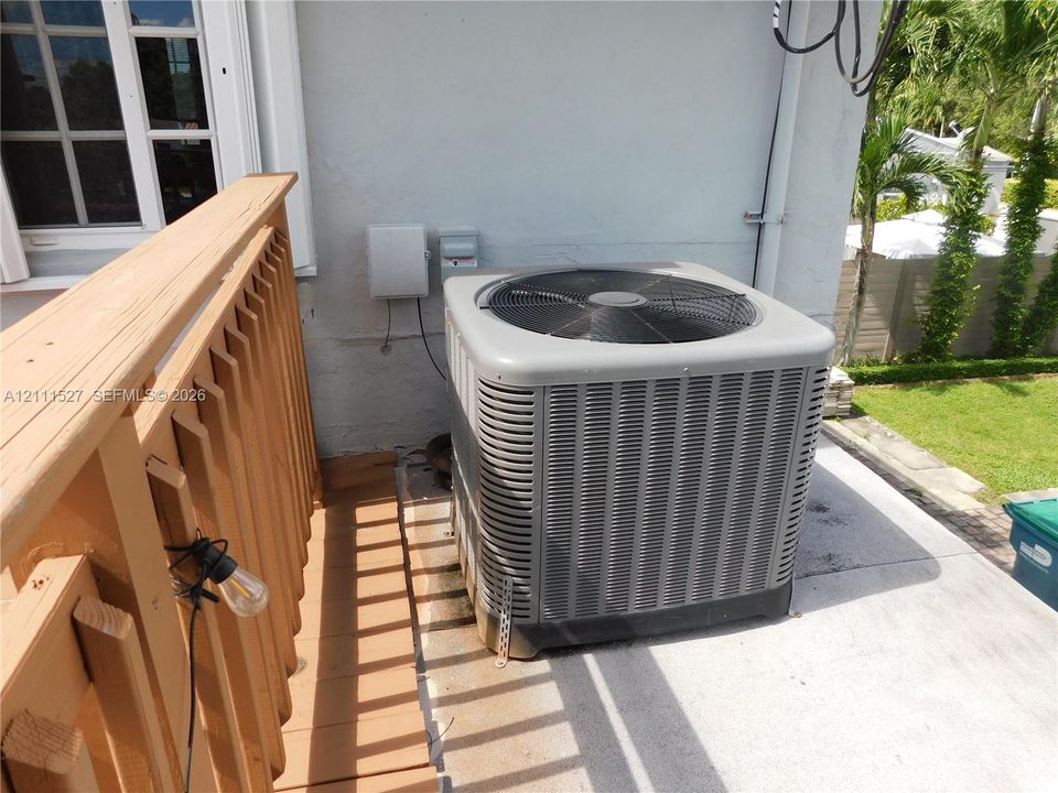 Exterior HVAC unit, wooden deck railing, and concrete patio surface