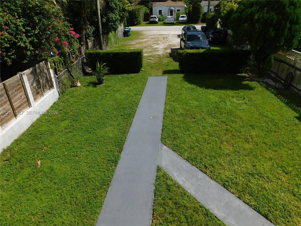 Backyard featuring a manicured lawn, concrete hardscaping, wood fencing, and perimeter hedging