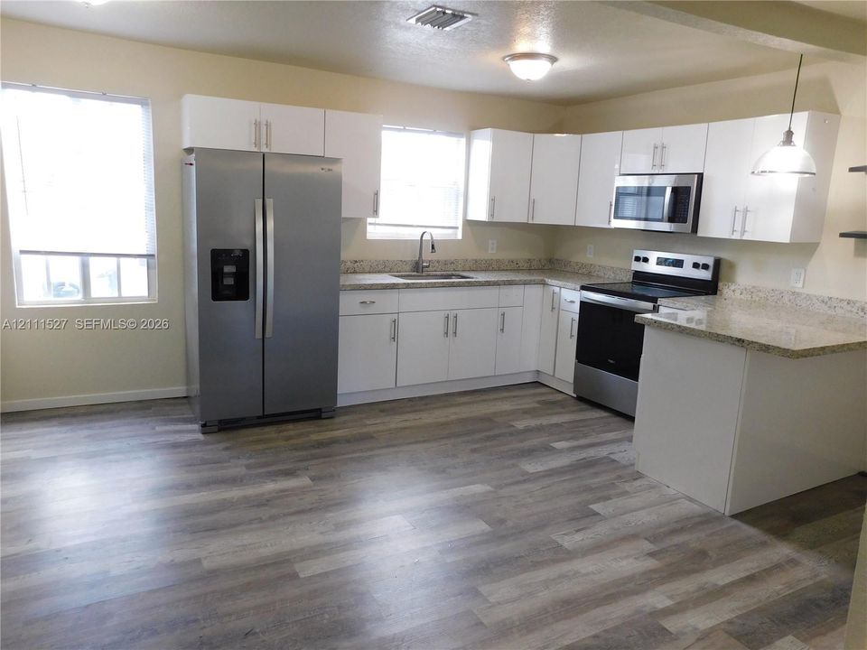Kitchen featuring white cabinetry, stone-finish countertops, stainless steel appliances, and wood-finish flooring