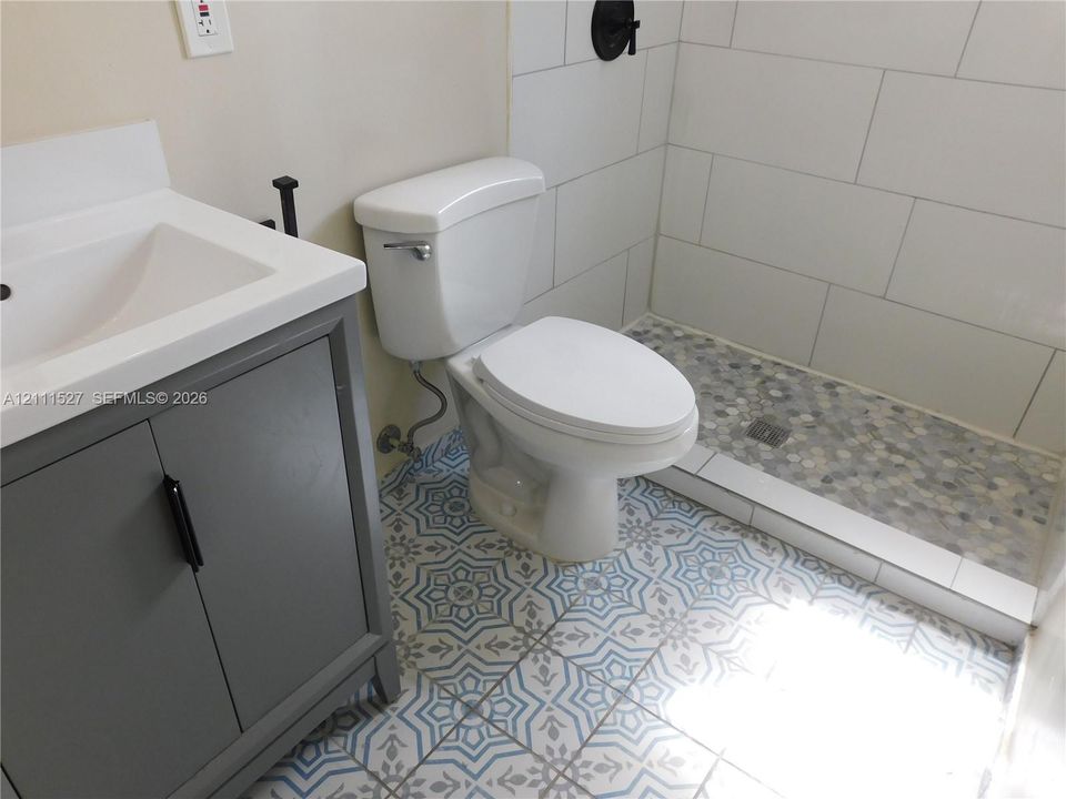 Bathroom featuring a grey vanity with a white countertop, patterned floor tile, and a walk-in shower with white subway tile walls and pebble-style floor tile