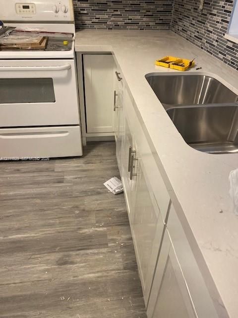 Kitchen featuring white shaker-style cabinetry, solid-surface countertops, dual-basin stainless steel sink, multi-tone linear tile backsplash, and wood-finish flooring