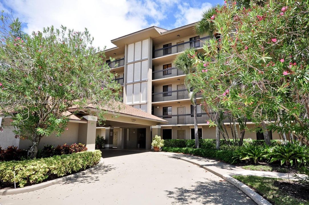 Multi-story exterior featuring a covered porte-cochère, private balconies with railings, and mature landscaping