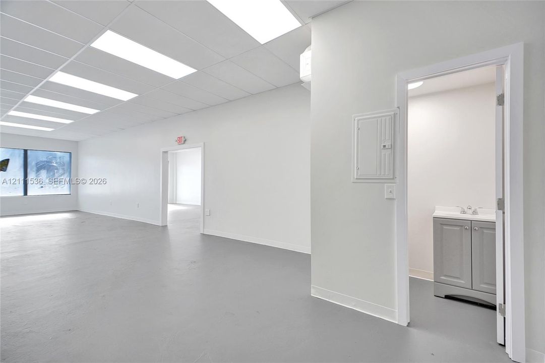 Open floor plan featuring recessed drop-ceiling lighting, smooth finished flooring, and a private restroom with a vanity cabinet