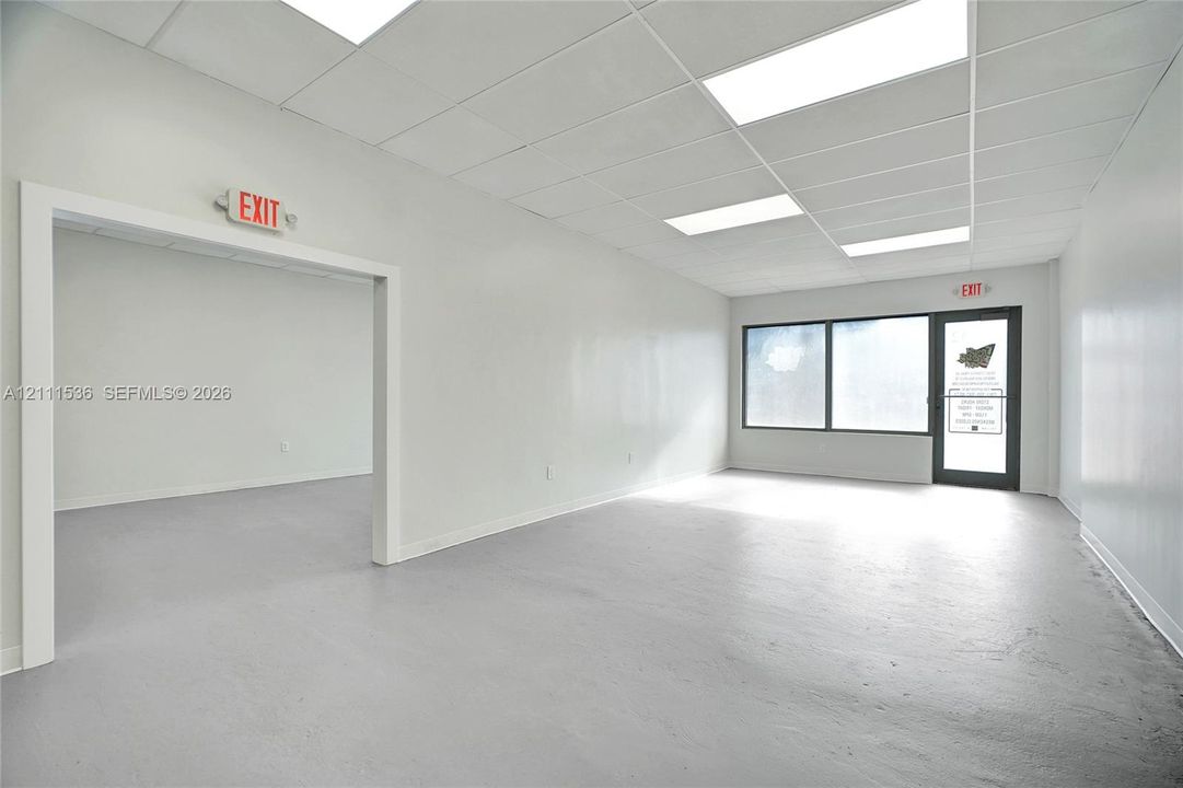 Open floor plan featuring neutral paint, drop-tile ceiling with recessed fluorescent lighting, continuous concrete flooring, and large paneled storefront windows