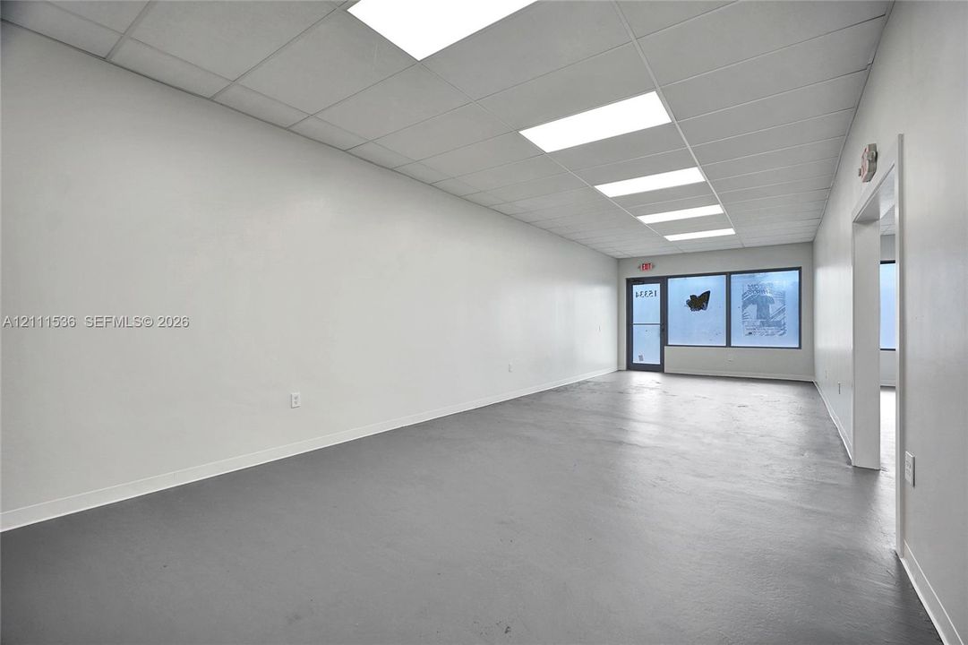 Open-concept interior featuring painted concrete flooring, a drop-tile ceiling, recessed rectangular lighting fixtures, and a glass-paneled storefront entry