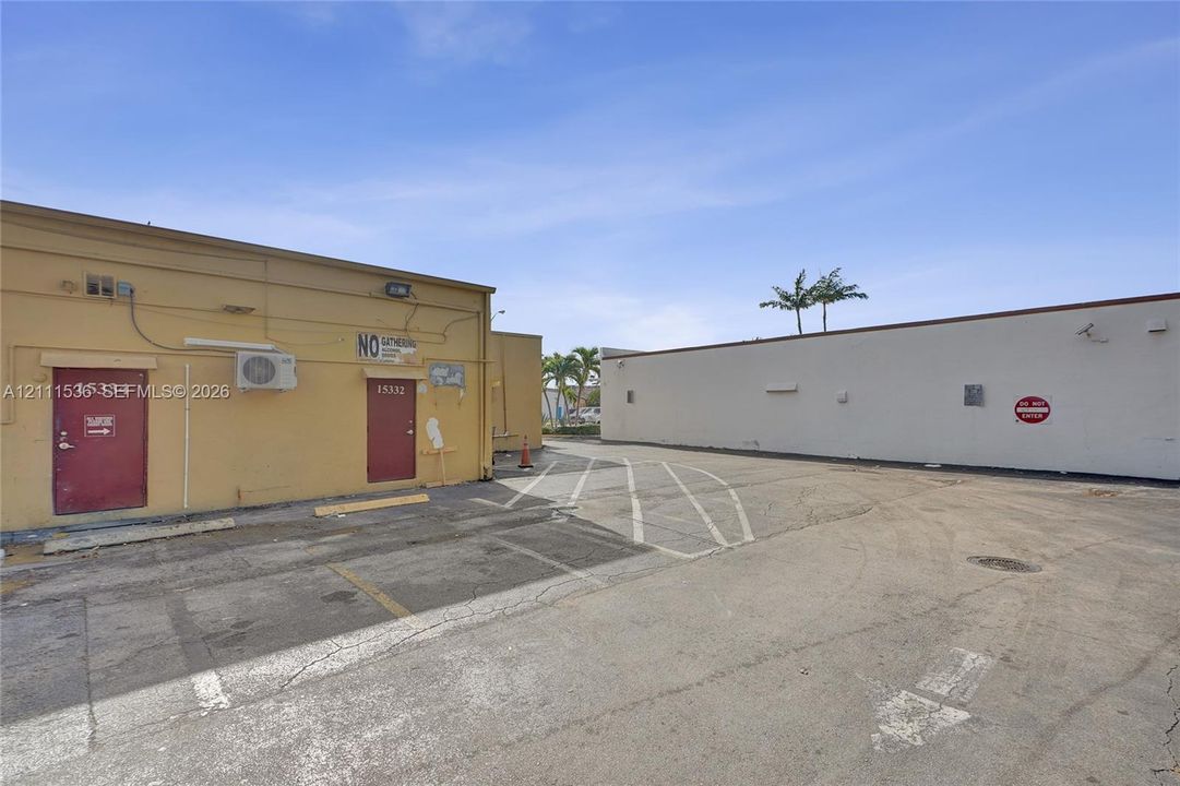 Asphalt-paved exterior area featuring marked parking spaces, exterior wall-mounted lighting, and painted masonry building façades