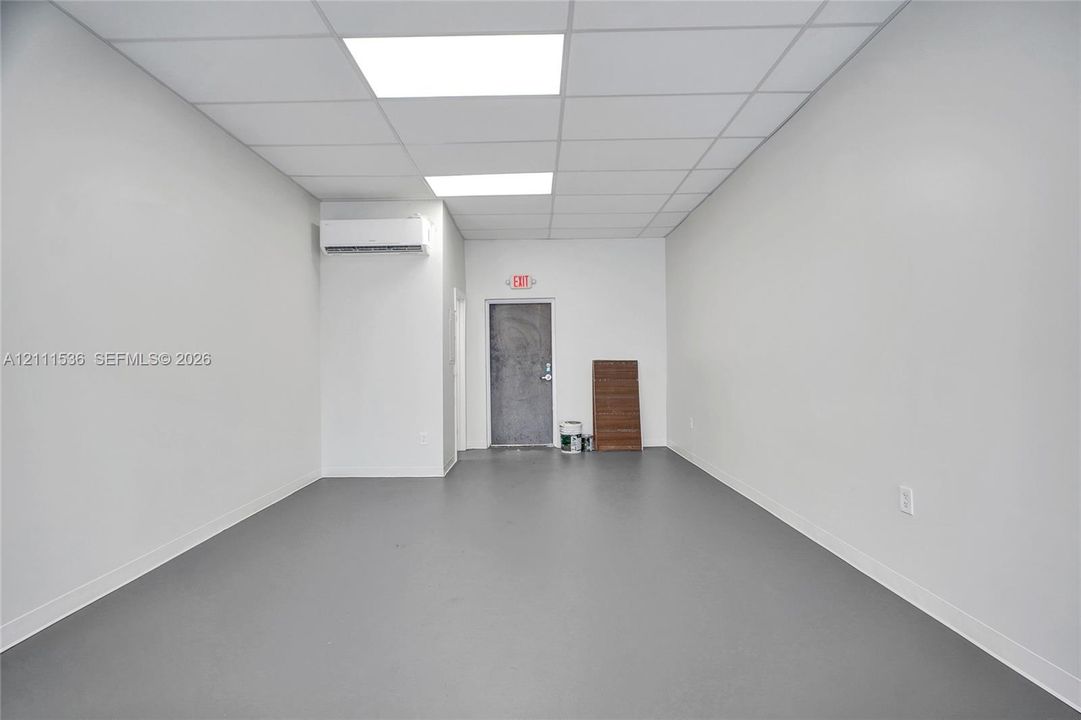 Interior room featuring high-durability grey flooring, white walls, recessed ceiling grid lighting, and a wall-mounted ductless heating and cooling unit