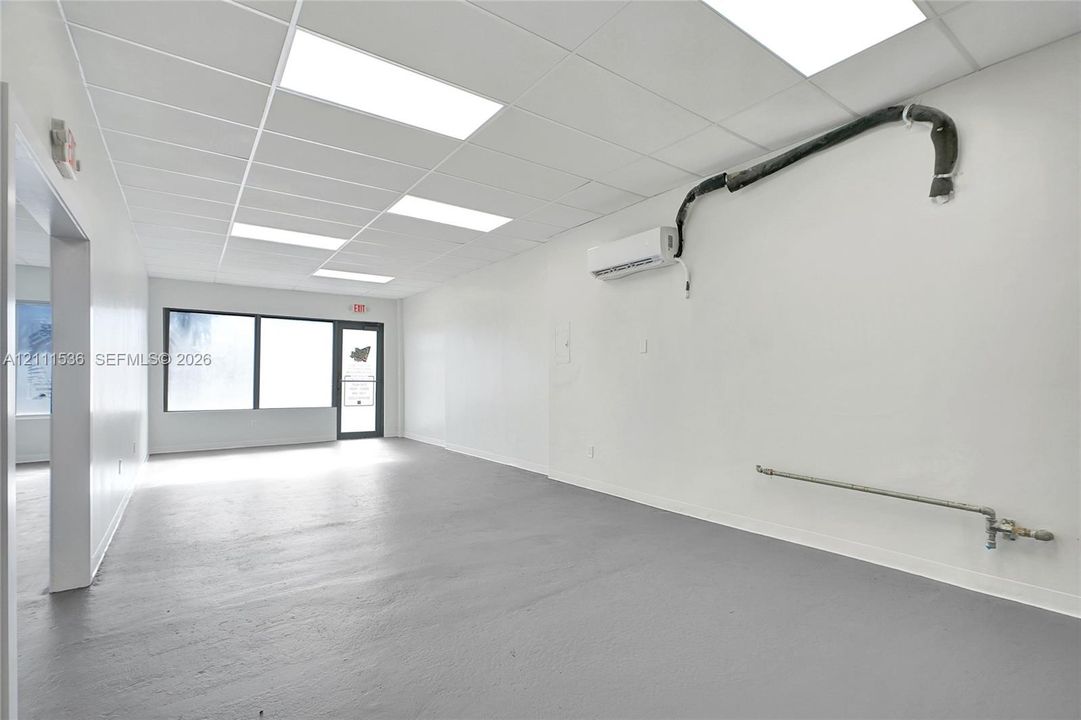 Open interior space featuring a drop ceiling with recessed lighting, smooth-finished flooring, wall-mounted climate control unit, and expansive storefront-style windows