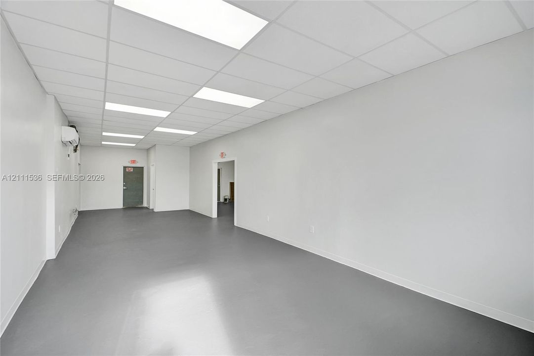 Open-concept interior featuring smooth-finish flooring, a suspended acoustic tile ceiling, recessed panel lighting, and wall-mounted climate control unit