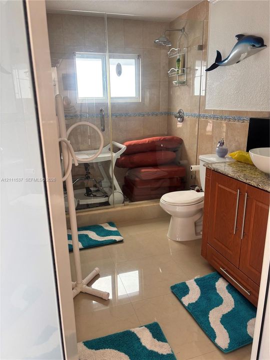 Bathroom featuring floor-to-ceiling tiled walls with decorative mosaic inlay, walk-in shower with frameless glass enclosure, wood-finish vanity cabinet, stone-finish countertop, and vessel sink