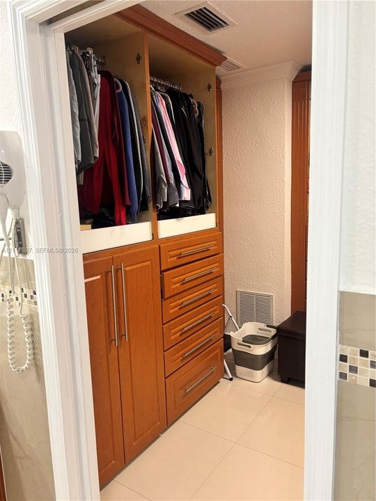 Custom wood-finish cabinetry featuring integrated shelving, hanging rods, and a six-drawer stack with metallic hardware, complemented by ceramic tile flooring