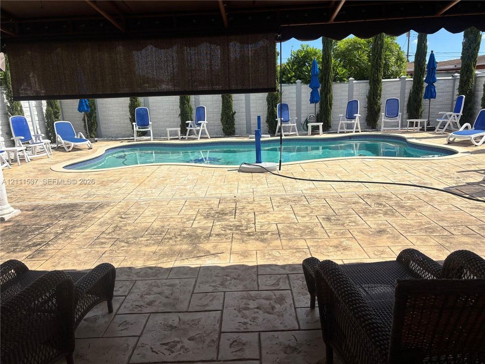 Backyard featuring a stamped concrete patio, in-ground swimming pool, masonry perimeter wall, and vertical landscaping accents